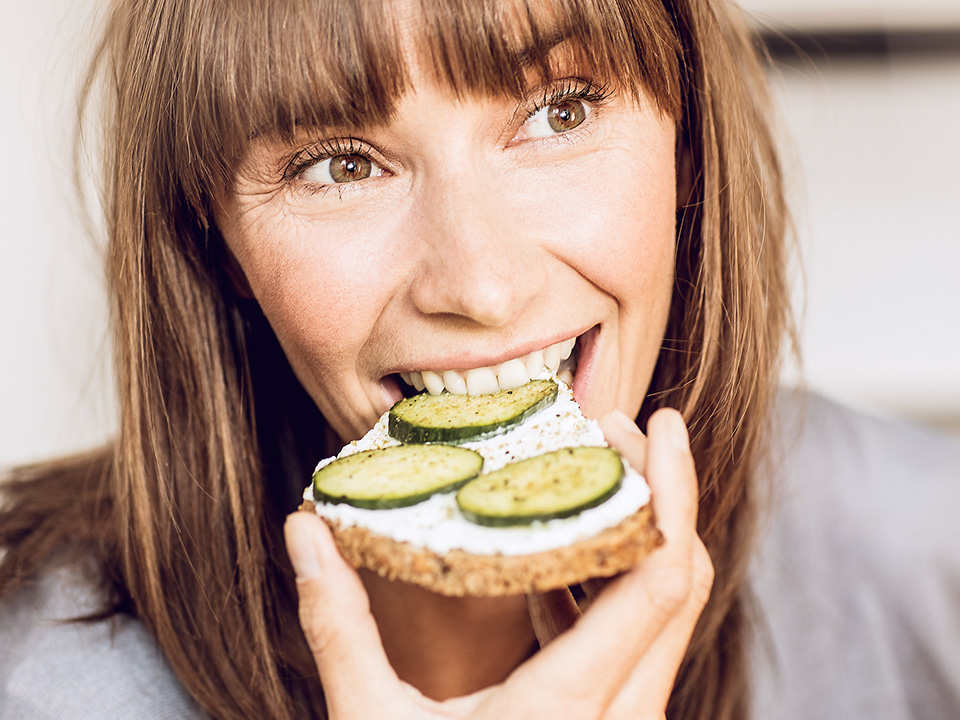 Frau beisst in ein gesundes Brot mit Gurken und Frischkäse
