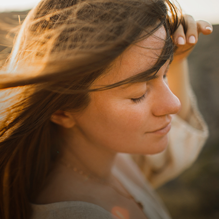 Frau mit geschlossenen Augen weht Wind ins Gesicht